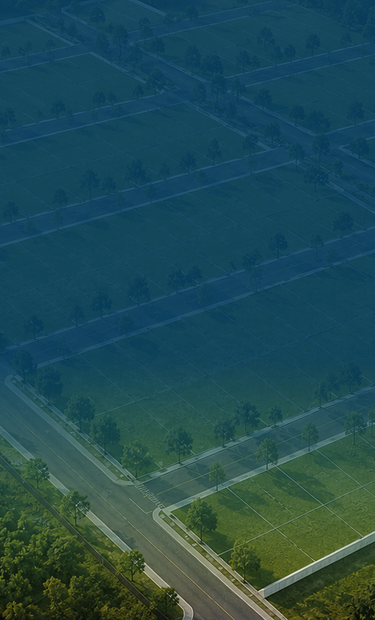 Vista aérea de um loteamento mostrando lotes verdes organizados em quadras, ruas pavimentadas e arborizadas, cercado por vegetação